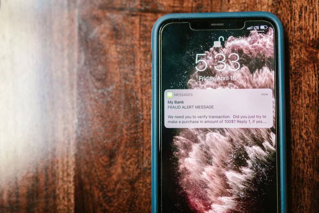 Smartphone affichant un SMS de faux livreur avec la photo d'un colis, posé sur un bureau, ambiance sobre